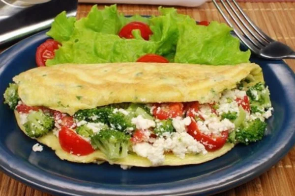 crepioca de brócolis com salada verde e tomates em um prato azul - Metrópoles