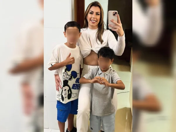 Imagem de mulher de calça jeans e blusa branca entre dois meninos - Metrópoles