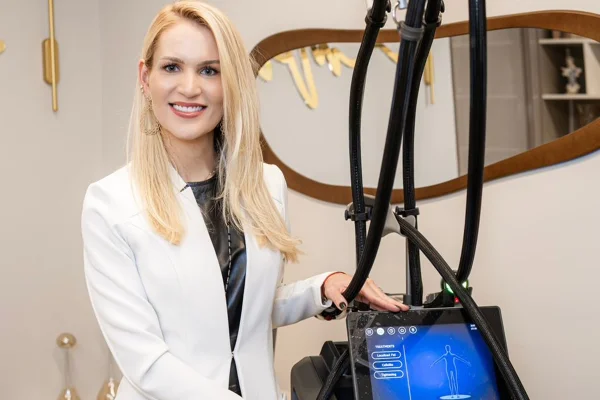 Foto colorida de mulher com jaleco ao lado de máquina estética - Metrópoles