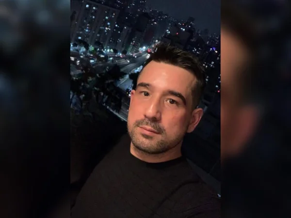 Foto colorida mostra Leonardo Severo em selfie. Ele tem cabelo preto penteado para trás e pele branca e usa camiseta preta. Ao fundo, é possível ver prédios à noite