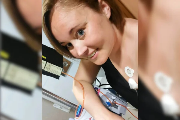 Imagem colorida de mulher vestida de preto com eletrodos no corpo enquanto posa para foto no hospital - Metrópoles