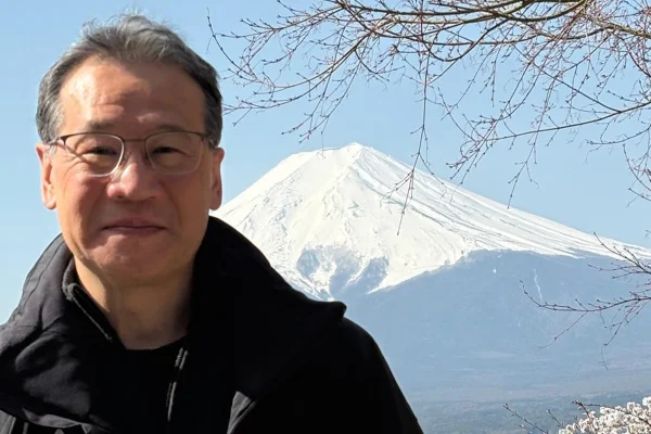 Foto colorida de homem asiático em ambiente ao aberto com montanha de neve atrás - Metrópoles.