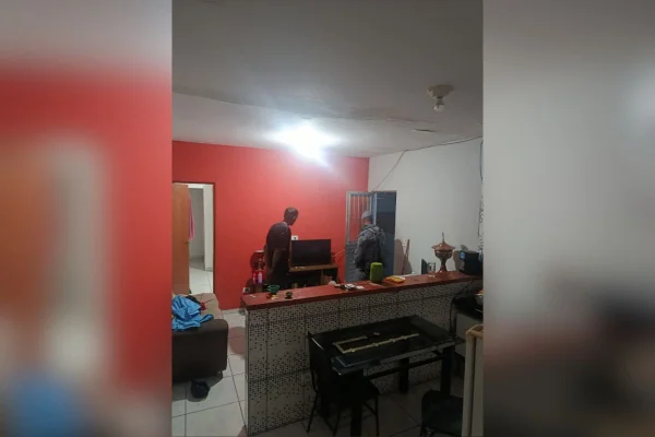 Foto colorida dentro de cômodo. Na imagem está um homem em pé e um policial militar.