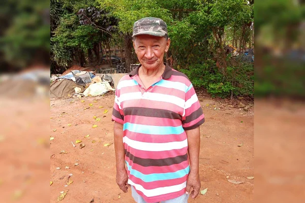 Homem parado em pé, em campo de barro com boné
