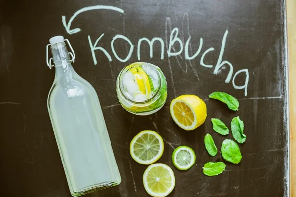 Foto colorida. Imagem mostra uma garrafa contendo um líquido branco e vários limões ao redor. A palavra Kombucha está escrita de giz - Metrópoles