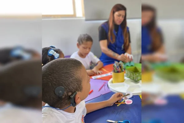 Criança com aparelho auditivo olhando para professora