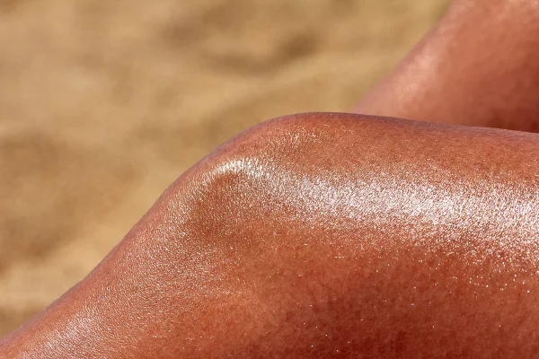 Close-up da perna de uma mulher muito bronzeada ao sol. Conceito de tanmaxxing. Metrópoles