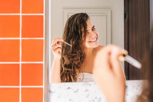 Foto colorida de mulher aplicando óleo no cabelo - Metrópoles