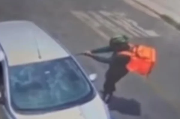 Imagem colorida de câmera de monitoramento de homem com mochila do ifood apontando arma - Metrópoles
