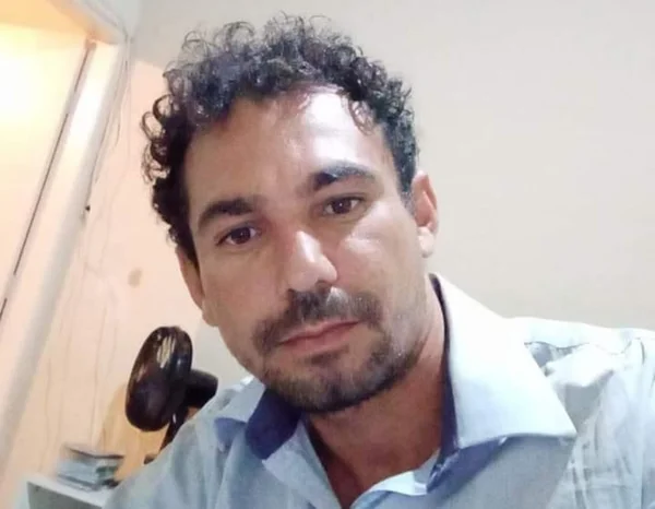 Imagem de homem vestindo camisa social azul claro com uma parede bege no fundo