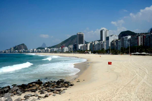 foto colorida de faixa de areia, mar e predios ao fundo - metrópoles