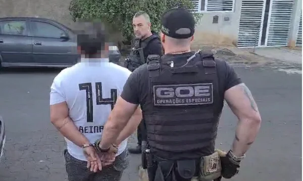 Em foto colorida policial conduz homem algemado. Ambos aparecem de costas, das quais na do policial aparece a sigla GOE, Operações Especiais - Metrópoles