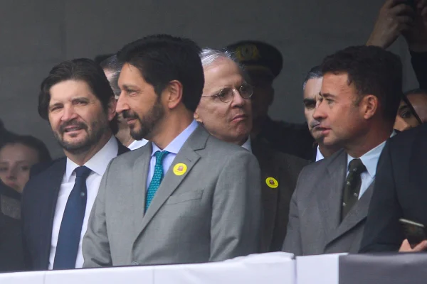 Imagem colorida mostra grupo de homens de terno e gravata em um palanque. No primeiro plano, Ricardo Nunes, homem branco, de cabelo e barba pretos,, vestindo terno cinza e gravata azul. Ele olha para seu lado direito e seu rosto está de perfil. Ele sorri - Metrópoles