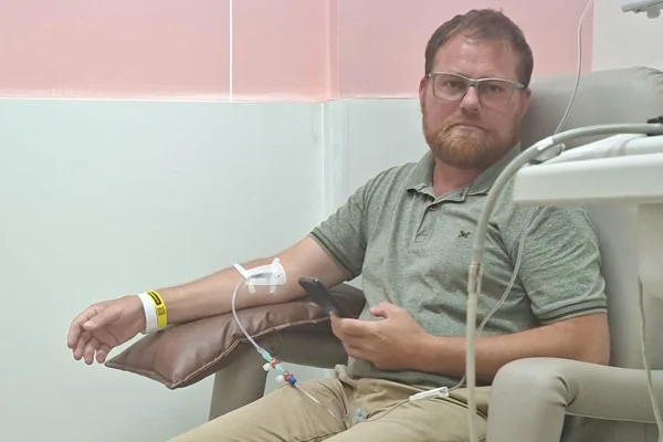 Foto colorida de homem em ambiente hospitalar com tubos de medicação conectados ao seu braço - Metrópoles.