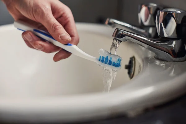 Foto colorida de pessoa molhando a escova de dente - Troca de escova de dente: saiba quando e por que é importante - Metrópoles