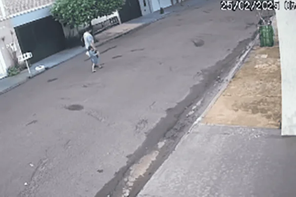 Imagem colorida de um homem adulto andando de mãos dadas com um menino em uma rua - Metrópoles