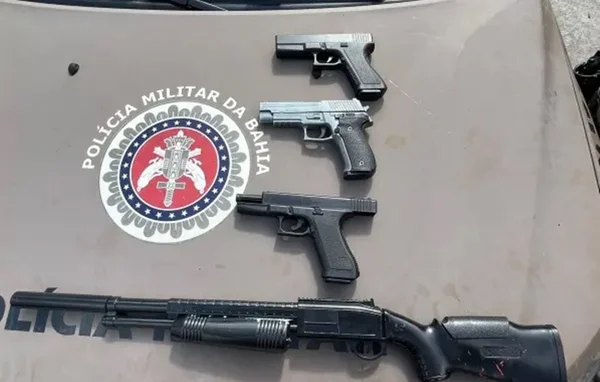 Três pistolas e uma escopeta enfileiradas em cima do capô de uma viatura da PM-BA - Metrópoles