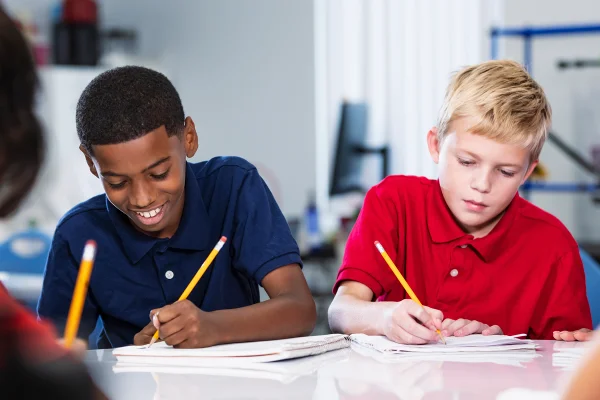 Imagem mostra dois meninos, um branco e outro negro, escrevendo em um papel - Metrópoles