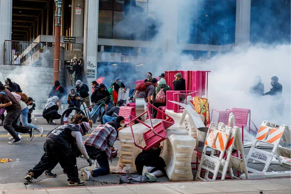 Foto colorida de policiais de Los Angeles disparando gás lacrimogêneo enquanto avançam sobre manifestantes que formaram uma barricada improvisada no centro da cidade durante um protesto contra batidas de imigração em 8 de junho de 2025 em Los Angeles, Califórnia - Metrópoles