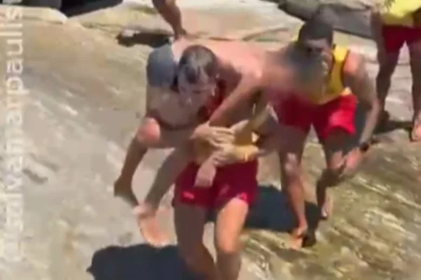 Imagem colorida de guarda-vidas com adolescente nas costas. Metrópoles