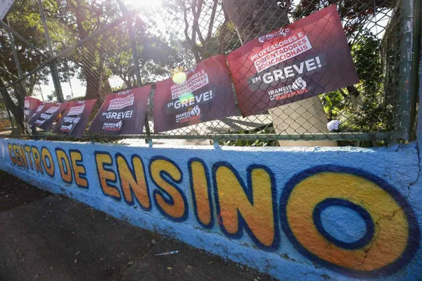 Grade de portão fechada em escola da rede pública. Cartaz de greve dos professores