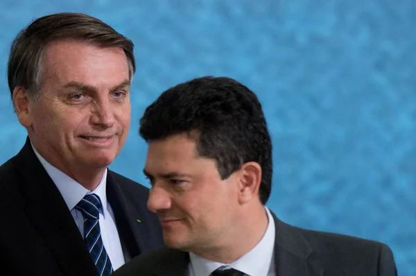 Na imagem colorida, dois homens estão centralizados. Eles usam terno e gravada escuro, possuem cabelo curto e ambos são brancos