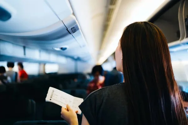 Imagem de mulher dentro de um avião, segurando uma passagem aérea - Metrópoles