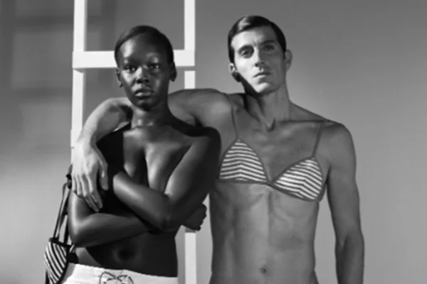 Na imagem em preto e branco, homem usa biquíni e mulher nada na parte de cima