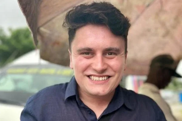 Foto colorida de homem sorrindo, vestindo camiza azul escura - Metrópoles.