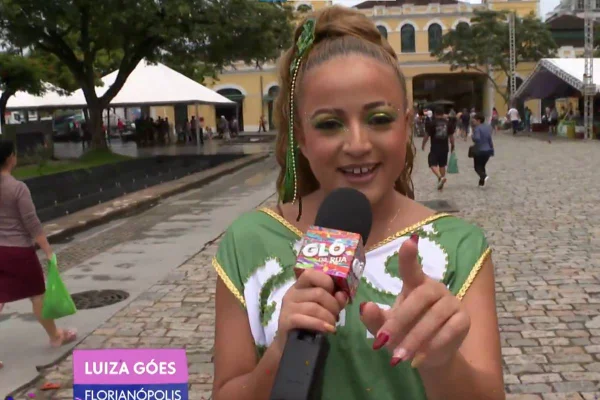 Foto colorida de Luiza Góes, repórter da Globo em matéria na rua, segurando microfone e falando com a câmera - Metrópoles