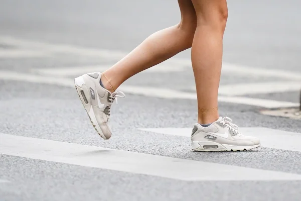 Pessoa atravessando a faixa de pedestres com tênis Nike Air Max cinza e branco.
