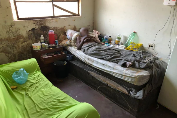 Homem deitado em cima de cama ao lado de diversos objetos e sujeira