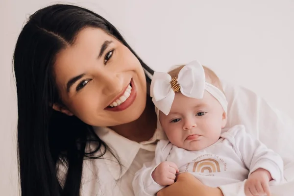 Foto colorida de mulher sorrindo segurando uma bebê recém nascida - Metrópoles.