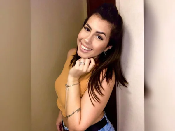 Imagem de mulher com cabelo preto e blusa amarela, sorrindo com a mão no queixo - Metrópoles