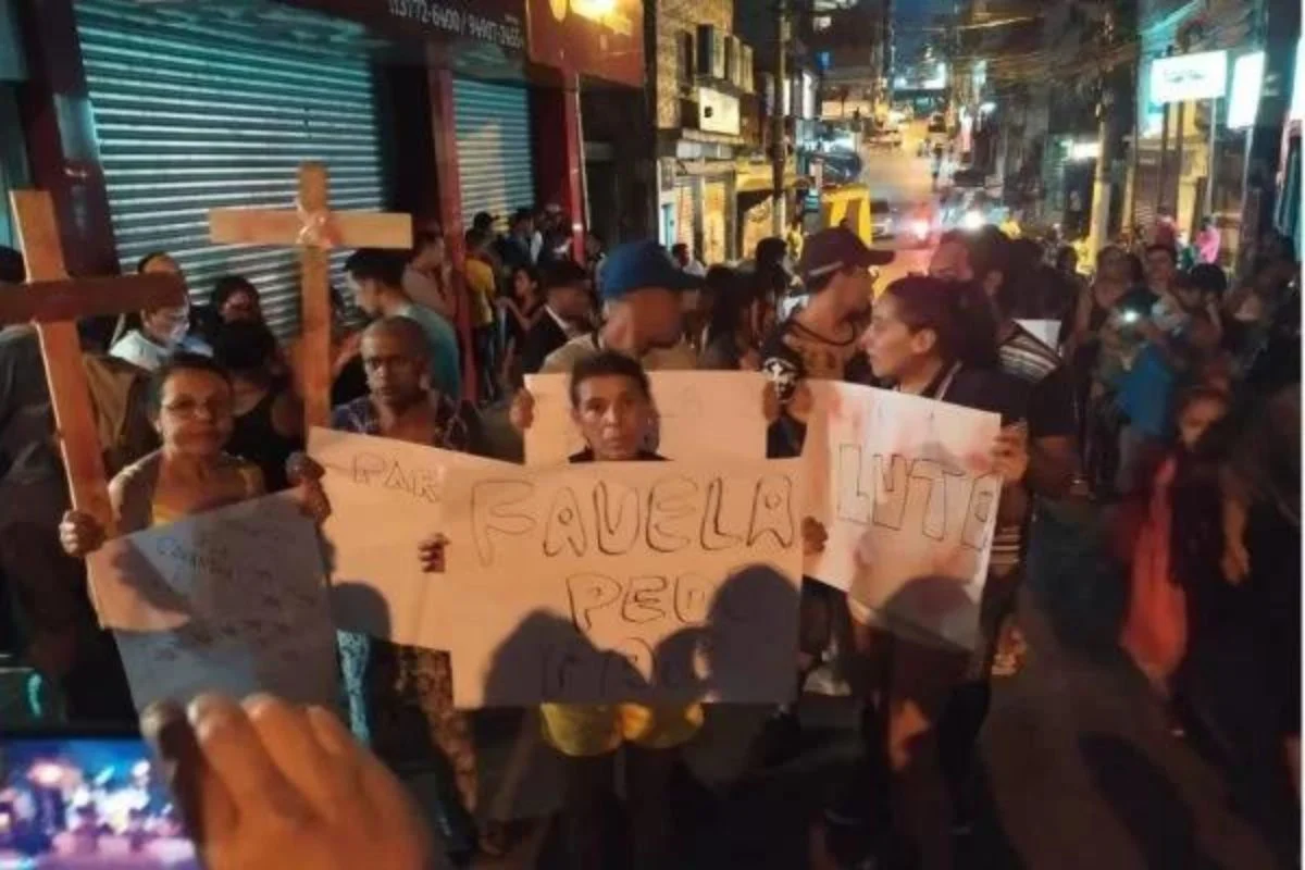 Imagem colorida de protesto em Paraisópolis, na zona sul de São Paulo. Pessoas aparecem segurando cartazes e cruzes - Metrópoles