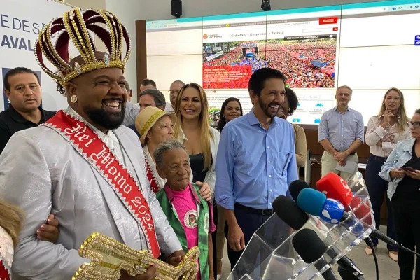 Imagem colorida mostra Ricardo Nunes, de camisa azul, com o rei momo do Carnaval, evento com suspeita de superfaturamento, e outras pessoas - Metrópoles