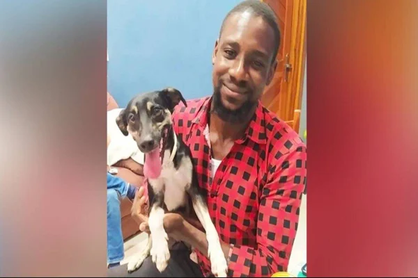 Foto colorida de um jovem, que veste uma blusa xadrez vermelha, segurando um cachorro-Metrópoles