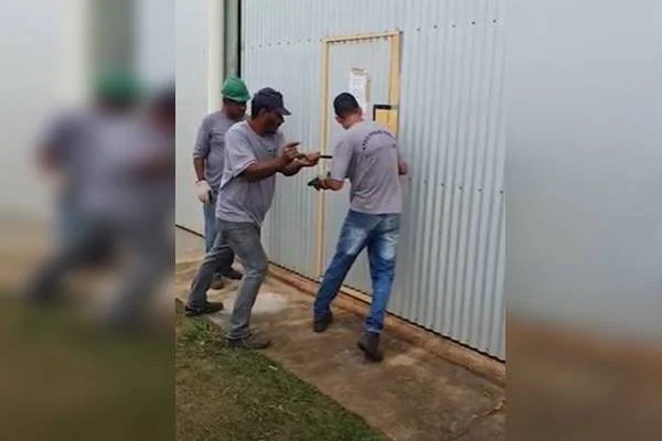 Três funcionários da Terracap uniformizados arrombam porta de hangares do Aeródromo Botelho, em São Sebastião, durante reintegração de posse - Metrópoles