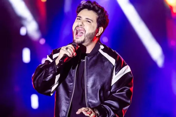 Thiago Carvalho em foto colorida. Ele está no palco, cantando em um microfone - Metrópoles