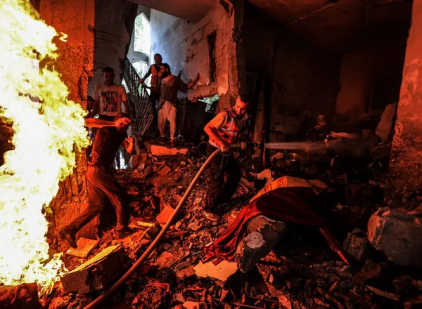 Imagem colorida de homens tentando apagar incêndio em construção na Faixa de Gaza - Metrópoles