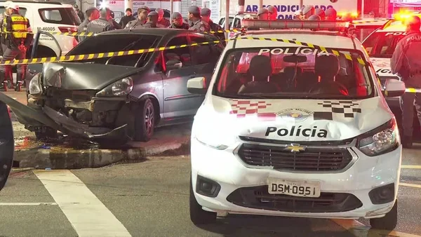 Dois carros estacionados em avenida; à frente, uma viatura branca da Polícia Militar de São Paulo; ao fundo, um carro cinza escuro com a parte frontal destruída - Metrópoles