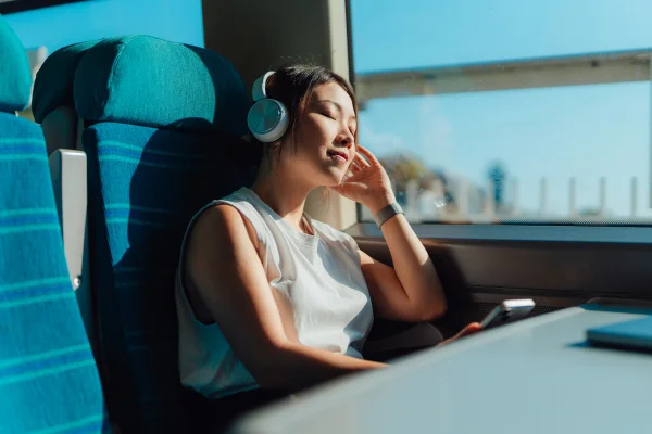 Jovem asiática com os olhos fechados, ouvindo música com fones de ouvido sem fio no trem. Metrópoles