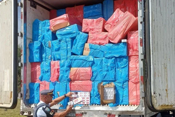 Imagem colorida de policial conferindo carreta com o baú aberto cheio de pacotes de cigarros - Metrópoles