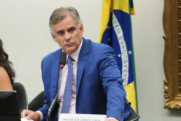 Imagem colorida mostra o deputado Leur Lomanto Júnior (União-BA). Ele veste um terno azul e atrás dele está uma bandeira do Brasil | Metrópoles