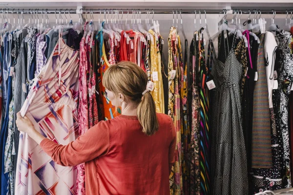 Mulher vestindo uma cardigan vermelho observa arara e segura uma peça