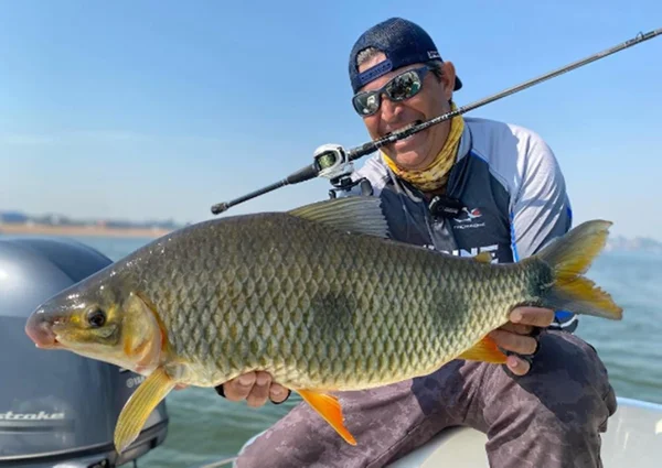 Imagem colorida de homem segurando um peixe após pesca esportiva - Metrópoles