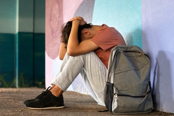 Imagem de jovem agachado e segurando a cabeça - Metrópoles