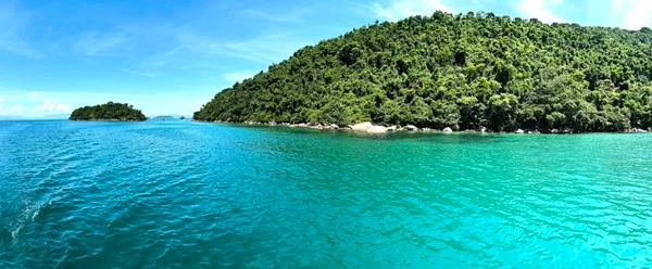 Mar azul com monte cheio de árvores no fundo - Metrópoles