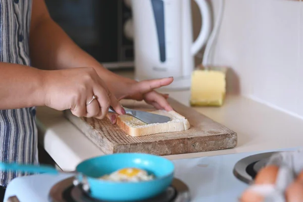 Foto colorida de uma mulher passando margarina no pão - Metrópoles
