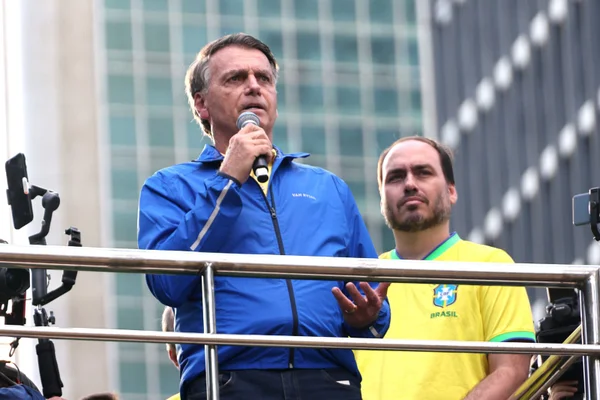 Jair Bolsonaro em manifestação Avenida na Paulista. Vestido de azul, ele segura um microfone. Atrás está um dos filhos do ex-presidente, Carlos Bolsonaro - Metrópoles